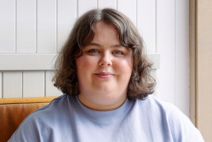 Comedian Taylor Griffiths smiling serenely with a timber clad wall behind her. 