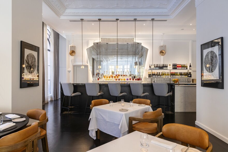 Elegant art-deco interior of a restaurant with dining tables covered in white linen, high ceilings and a large central bar area.