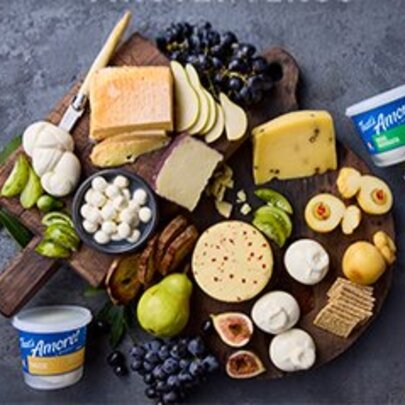 Looking down at an artisanal grazing platter featuring a variety of fresh Italian-style cheeses, tubs of curd and ricotta, grapes, pears, figs, and crackers arranged on a wooden board.