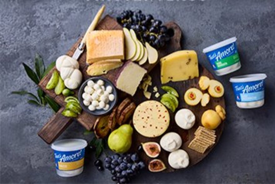 Looking down at an artisanal grazing platter featuring a variety of fresh Italian-style cheeses, tubs of curd and ricotta, grapes, pears, figs, and crackers arranged on a wooden board.
