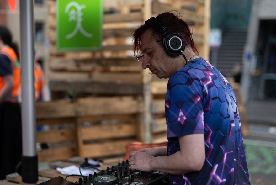 A DJ playing a live set in an outdoor setting with packing cases.