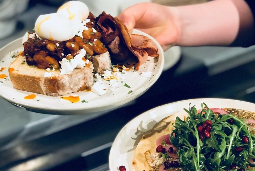 Eggs on toast and another dish with rocket and pomegranate seeds being carried.