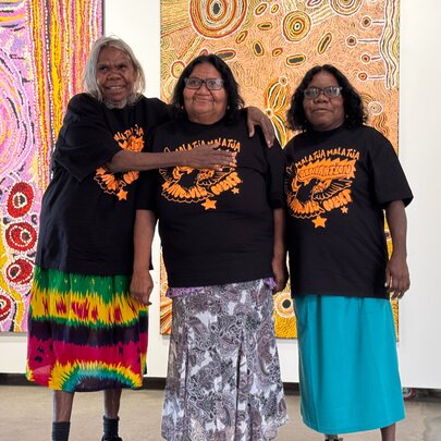 Three First Nations artists posing for a group shot in front of large artworks in a gallery.