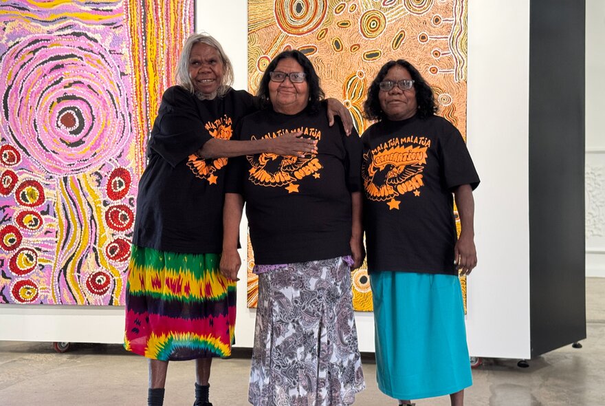 Three First Nations artists posing for a group shot in front of large artworks in a gallery.