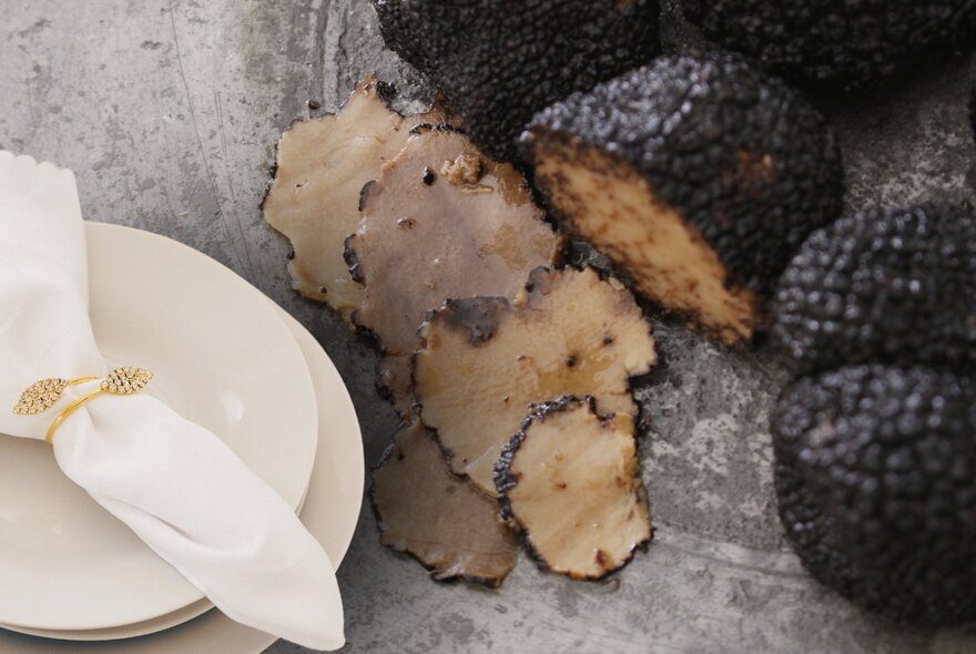 Thinly sliced black truffles on a board, next to a white plate.