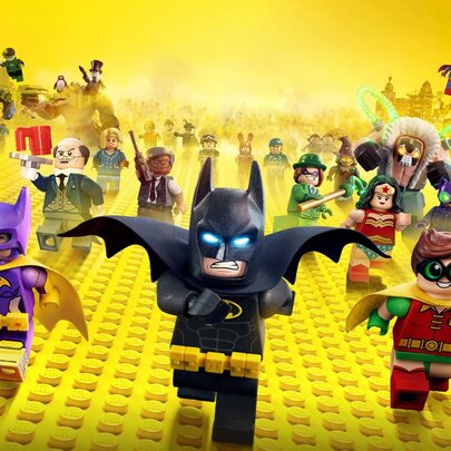 A scene from the Lego Batman movie showing Batman leaning a group of mini figures across a yellow Lego baseplate. 