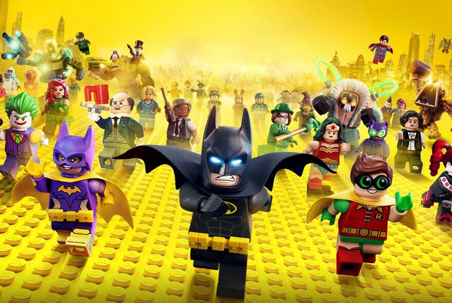 A scene from the Lego Batman movie showing Batman leaning a group of mini figures across a yellow Lego baseplate. 
