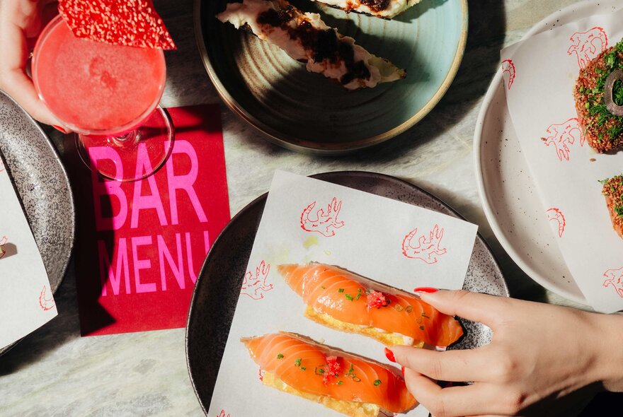 Hands reaching for food from a plate with bar menu.
