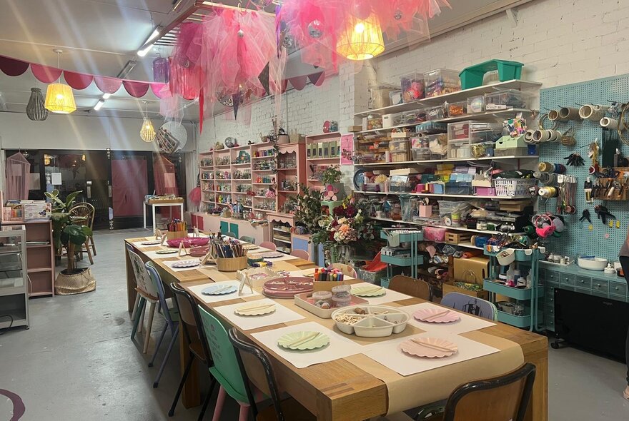 A long table set up for a party with decorations hanging from the ceiling and cluttered shelves in the background. 