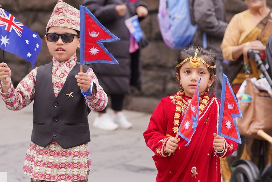 Two young children in Nepalese costumes, holding small flags in their hands, outdoors.