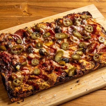 A rectangular pizza with crispy edges served on a wooden board.