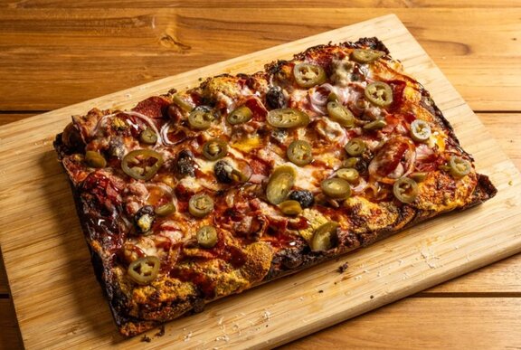 A rectangular pizza with crispy edges served on a wooden board.