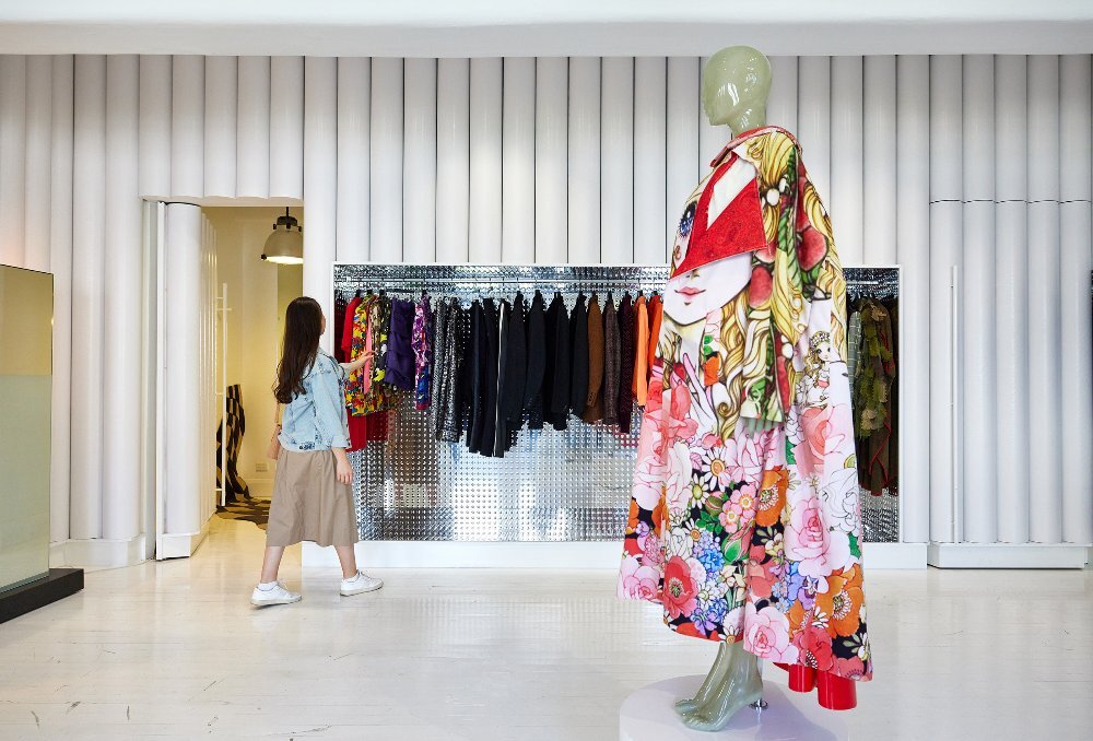 A woman is looking at clothes in a store. There is a mannequin wearing a kimono in the store.