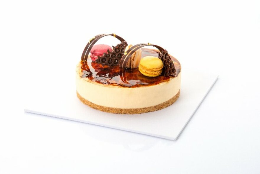 A cheesecake dessert with biscuit base, thick layer of cheesecake topped with glazed fruit and macarons.