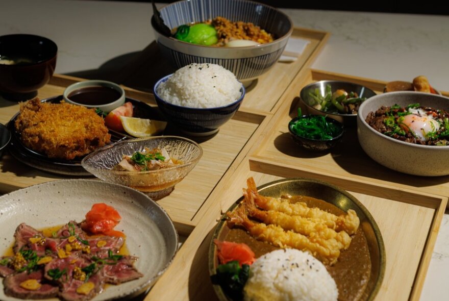 A table at Kuru restaurant filled with plates of Japanese food on bamboo trays.