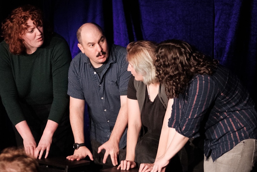 Four actors improvising live on a theatre stage in front of a black curtain.
