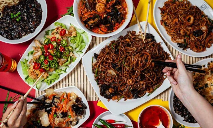 White plates and bowls on a table filled with fried noodle dishes, chicken salad, stew and stir fries.