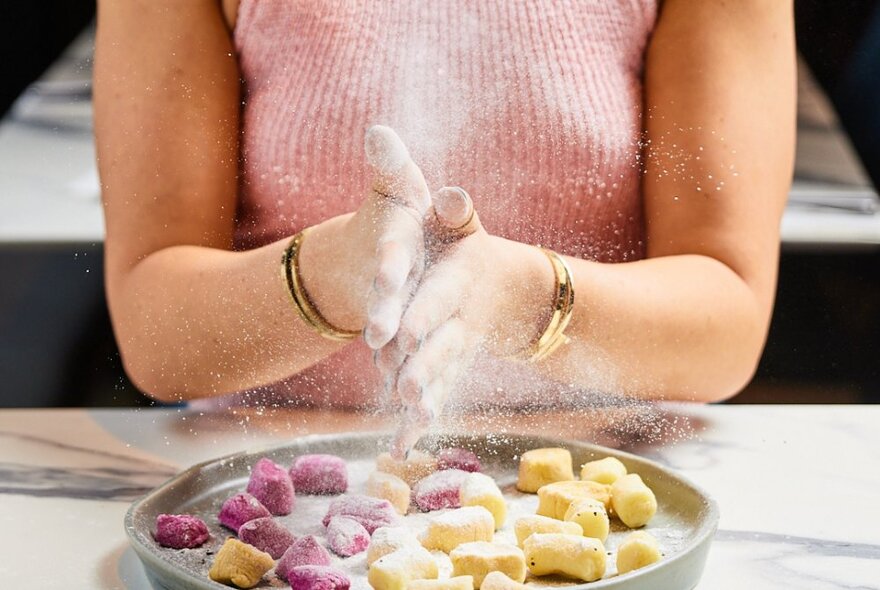 A woman brushing flour off her hands making gnocchi in traditional and beetroot colours. 