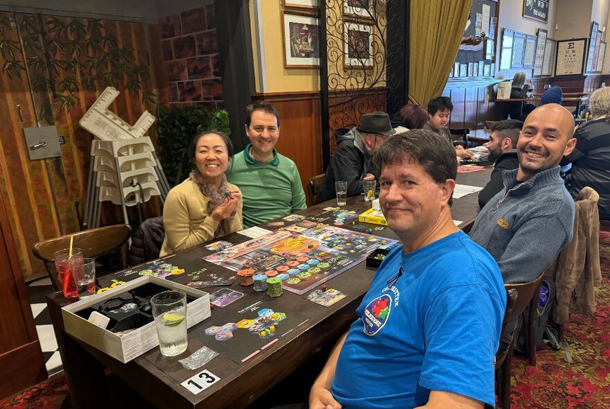A room inside a pub filled with people seated at tables and playing board games and smiling for the camera.