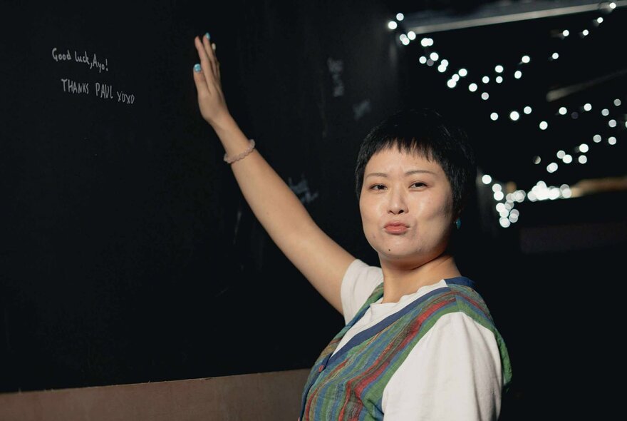 A woman with short hair, smiling and holding up her right arm as if waving.