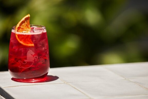 A red spritz in a short glass served with a slice of orange as a garnish.