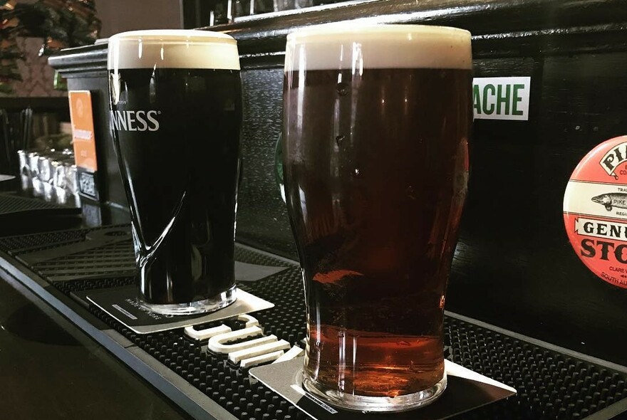 Two glasses of Guinness on a wooden bar with beer labels.