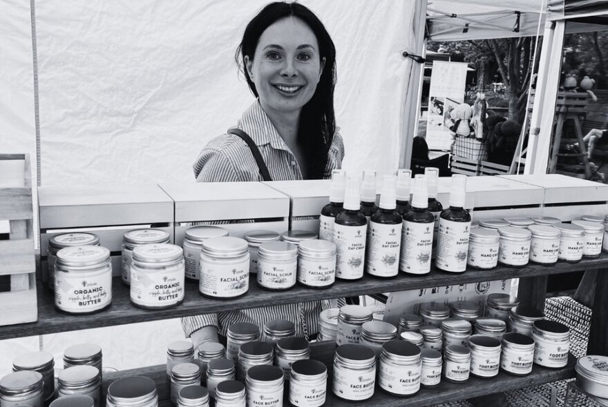 Woman looking over shelves of jars of produces at a market stall.