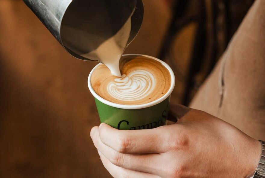 Hands holding a takeaway cup and pouring milk into coffee.
