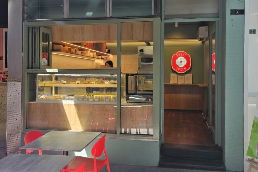 Laneway cafe with outdoor table seating, glass food counter inside with signage and ordering area.