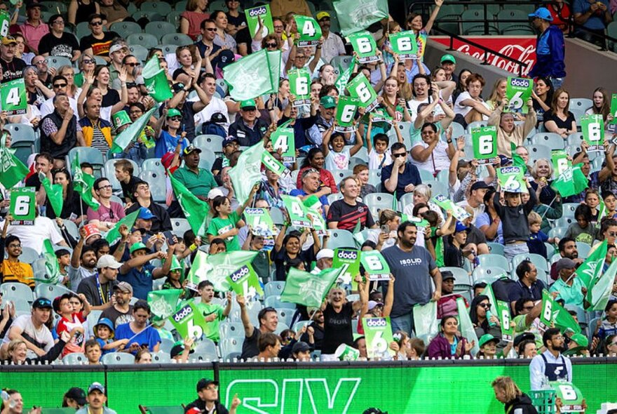 BBL Melbourne Stars supporters in the stands at the MCG, all wearing green and black and holding up large cards with '6' on them.