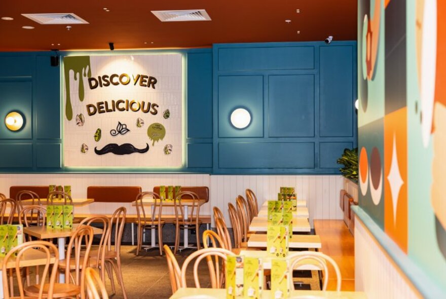 Interior of San Churro store at Southgate showing dining area with tables and chairs, blue wall and a sign on the back wall. 