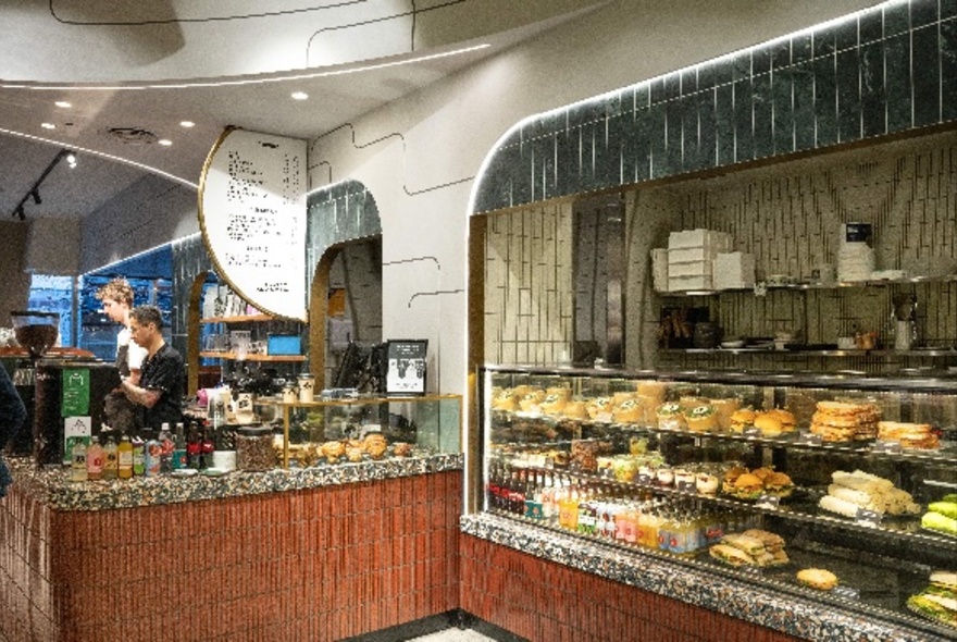 Interior of Axil Coffee at Collins Arch, with staff working behind the large service counter, a large display of food to the right in a glass cabinet.