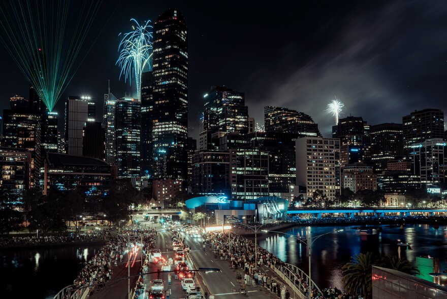 Fireworks above the Melbourne city skyline against a dark sky, with the Yarra river in the middle distance.
