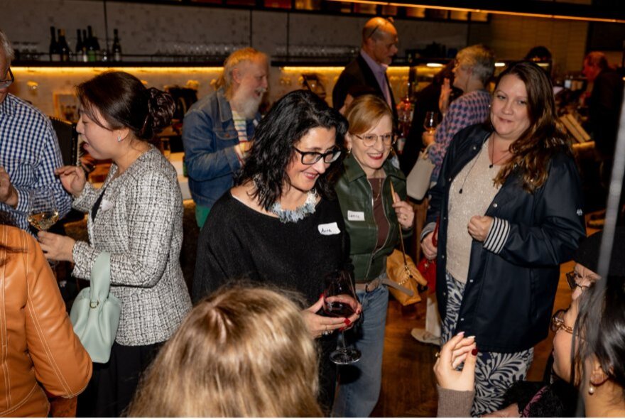 An indoor social gathering with people talking and holding drinks.