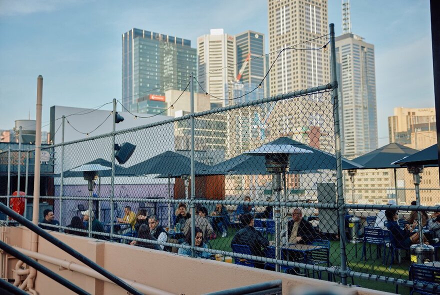 People enjoying drinks at a rooftop bar with cityscape in the background.