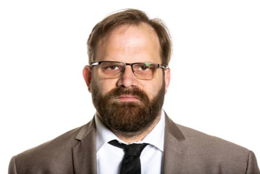 Bearded man with glasses, looking grumpy.