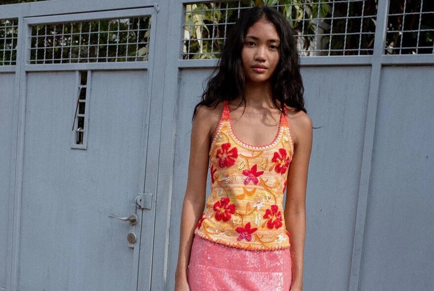 A woman is wearing a tank top with hibiscus flowers on it and she is wearing a pink sequin skirt