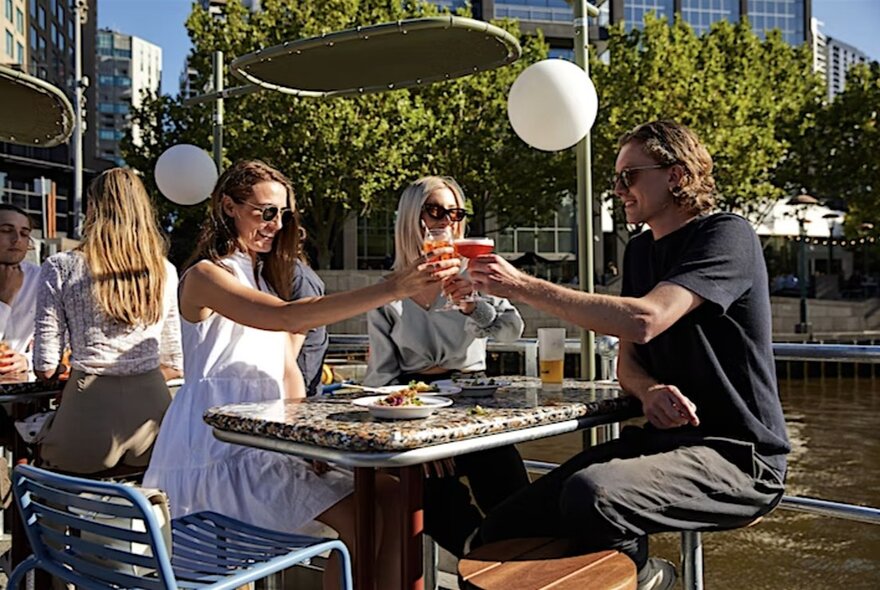 Three people clinking glasses at a table at Ponyfish Island.