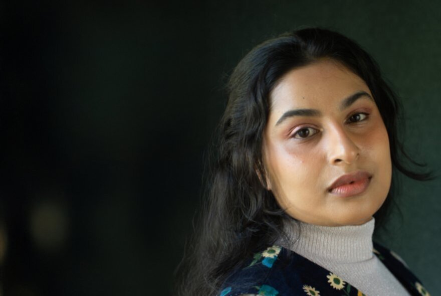 A  portrait of a person with straight dark hair against a dark background.