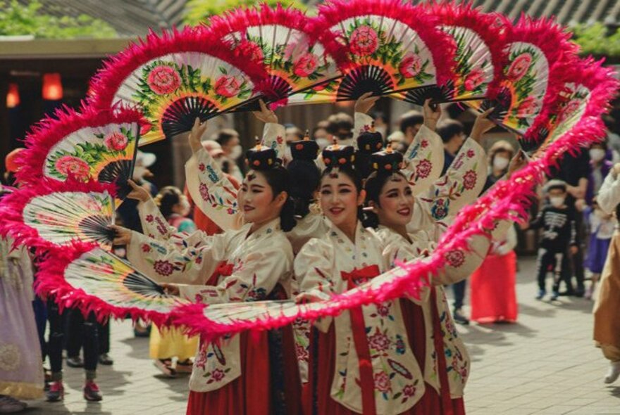 Korean dancers with fans forming an arced circle, wearing traditional dress.