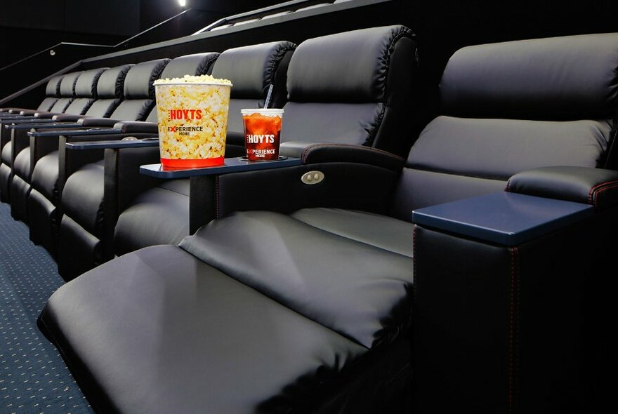 A row of empty reclining cinema seats with a bucket of popcorn and cup of Coke