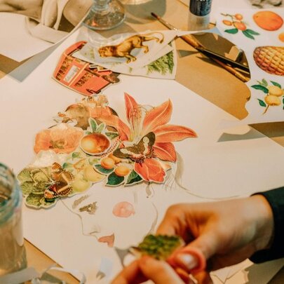 A close shot of hands working on a paper collage showing orange flowers. 