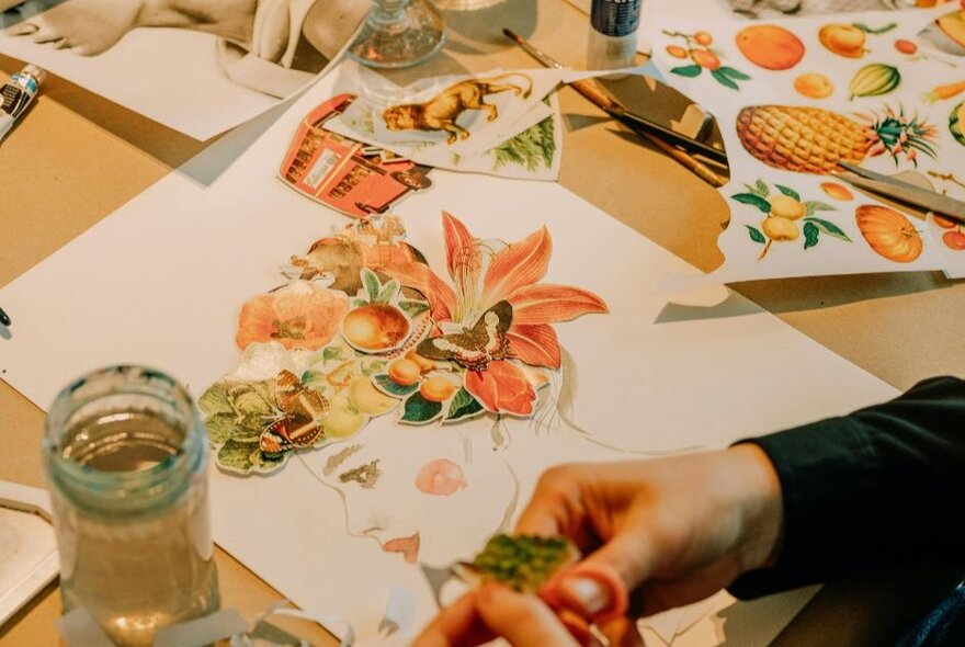 A close shot of hands working on a paper collage showing orange flowers. 