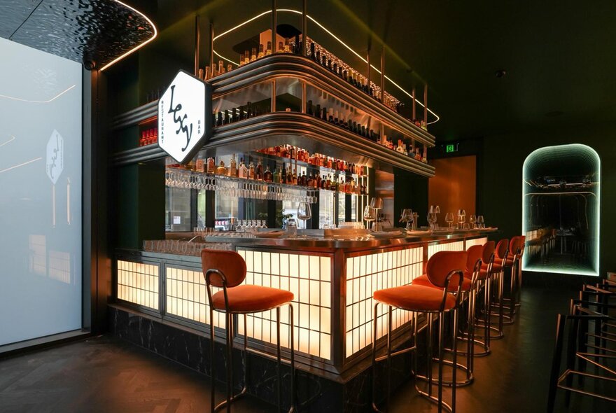 A dimly-lit bar lit up in soft lighting. There is a glowing sign above the bar that says Lexy.