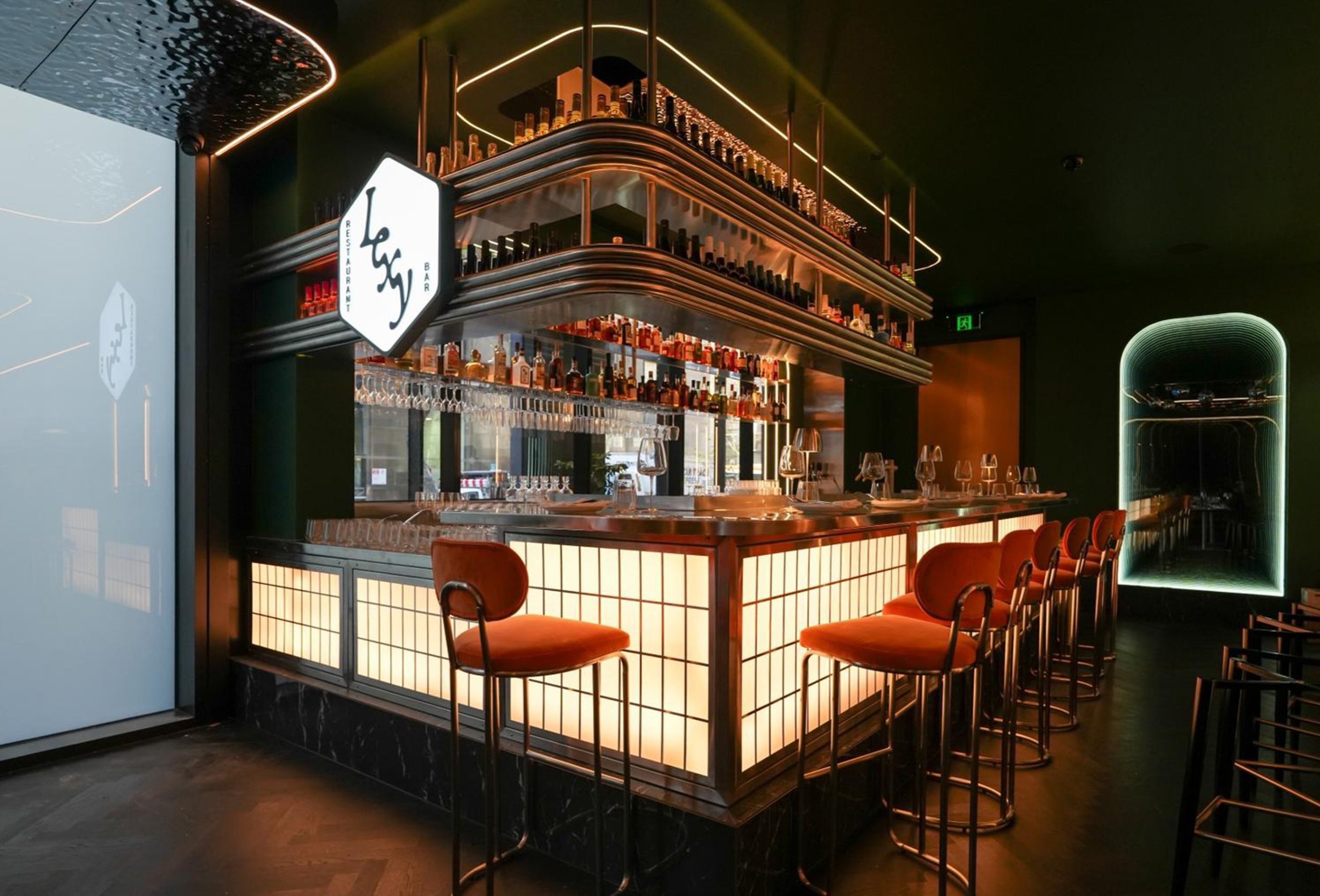A dimly-lit bar lit up in soft lighting. There is a glowing sign above the bar that says Lexy.