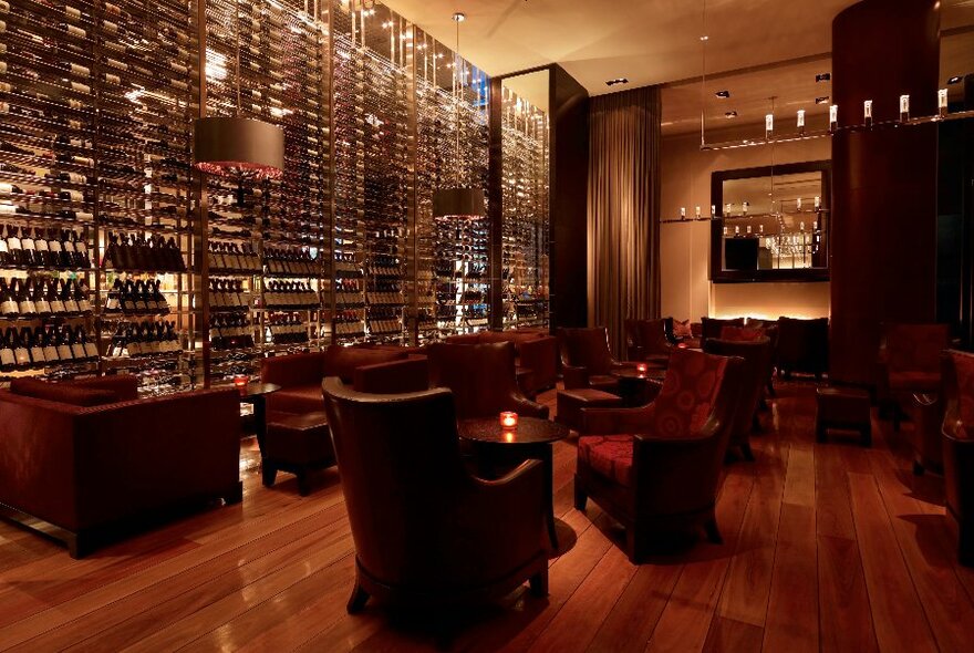 Interior of Ru-Co Bar showing large armchairs and club lounges arranged in front of a wall of shelves filled with bottles of wine and spirits.