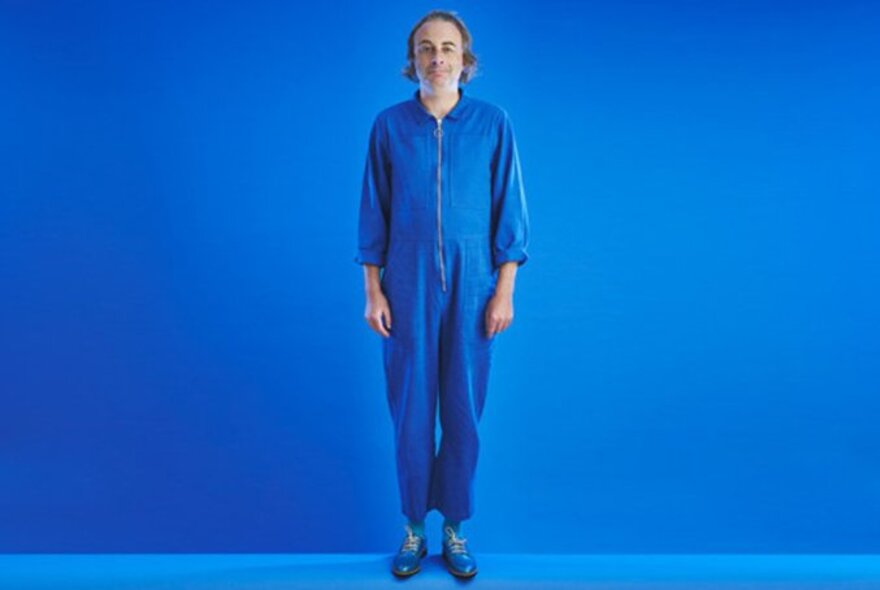 Comedian Paul Foot in an azure blue onesie with the same coloured background. 