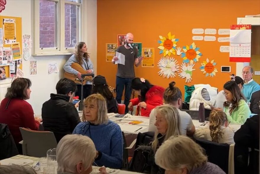 People attending a workshop in a small classroom setting with orange walls. 