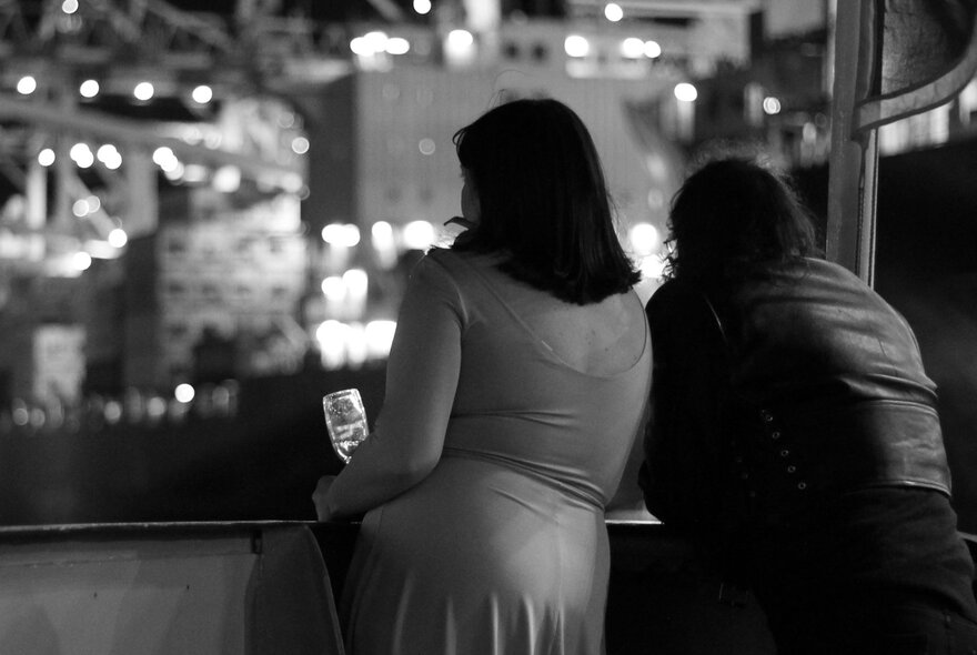 Couple standing at a shipboard railing at night, twinkling Docklands buildings in the background.