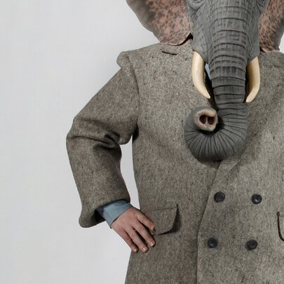 Mid-face downwards view of a creature in a grey overcoat with an elephant's head. 